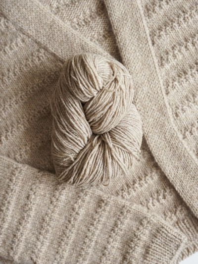 Beige merino wool yarn skein on knitted garment background